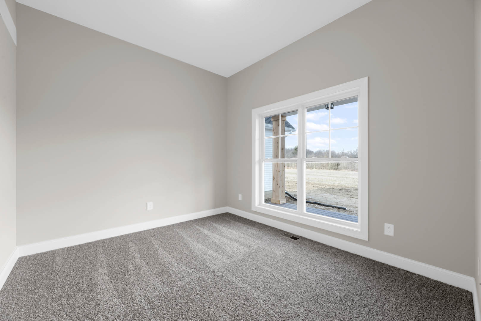 Bright room with white walls and ceiling, large window with white frame, grey carpeted floor, natural light illuminating interior