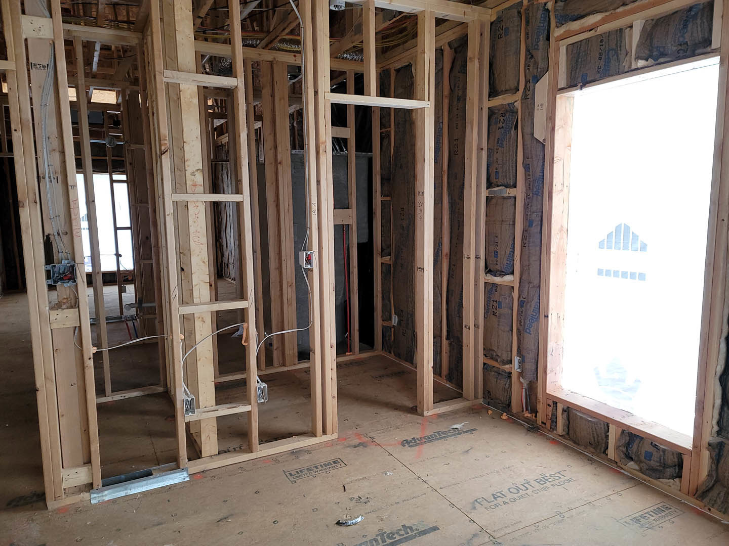 Wood-framed room under construction with exposed beams, unfinished floor, and a window displaying a sign