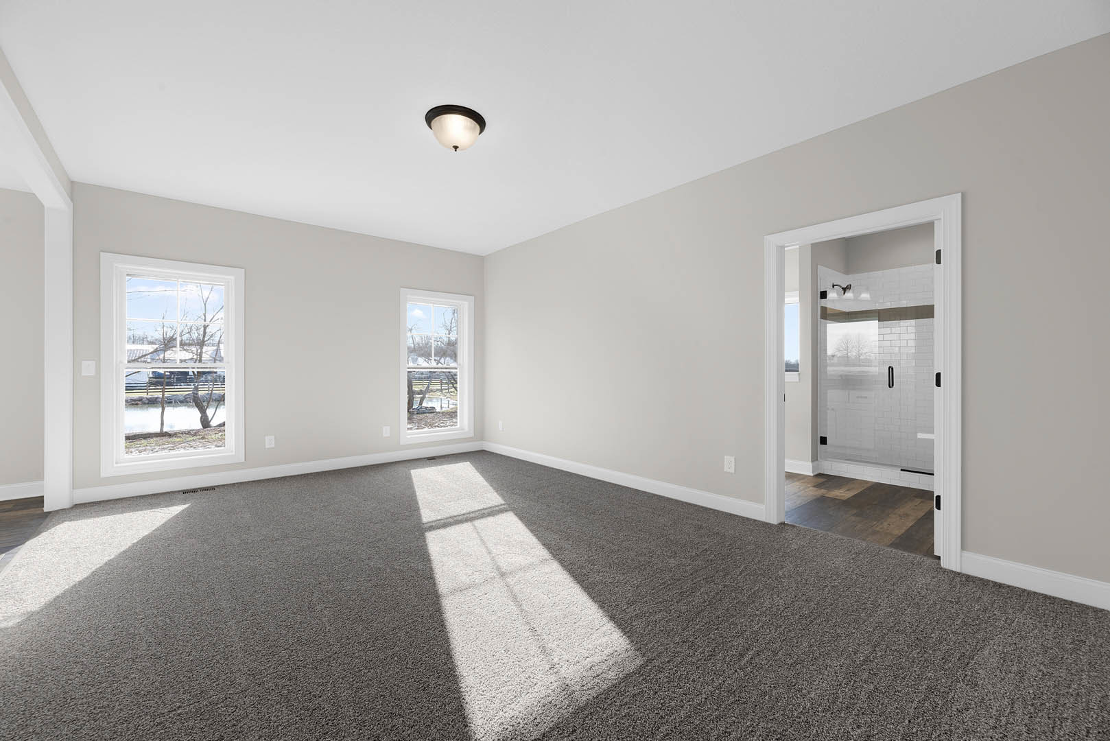 Carpeted room with open door, large windows, ceiling light fixture, and views of river, trees, and farmland