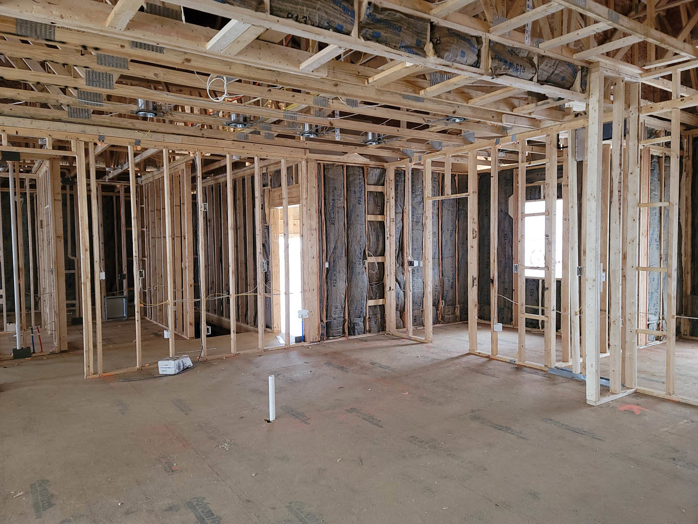 Room under construction with exposed wood framing, unfinished ceiling beams, and a white structural pole on a plywood subfloor