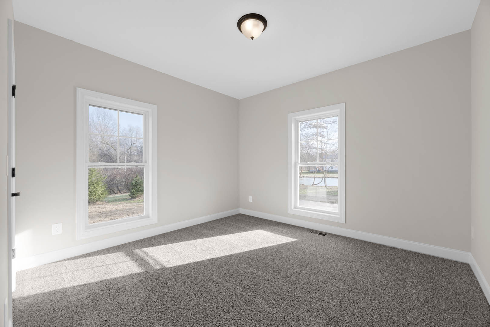Carpeted room with large windows, natural light streaming in, white walls, decorative molding, and a view of trees and river outside