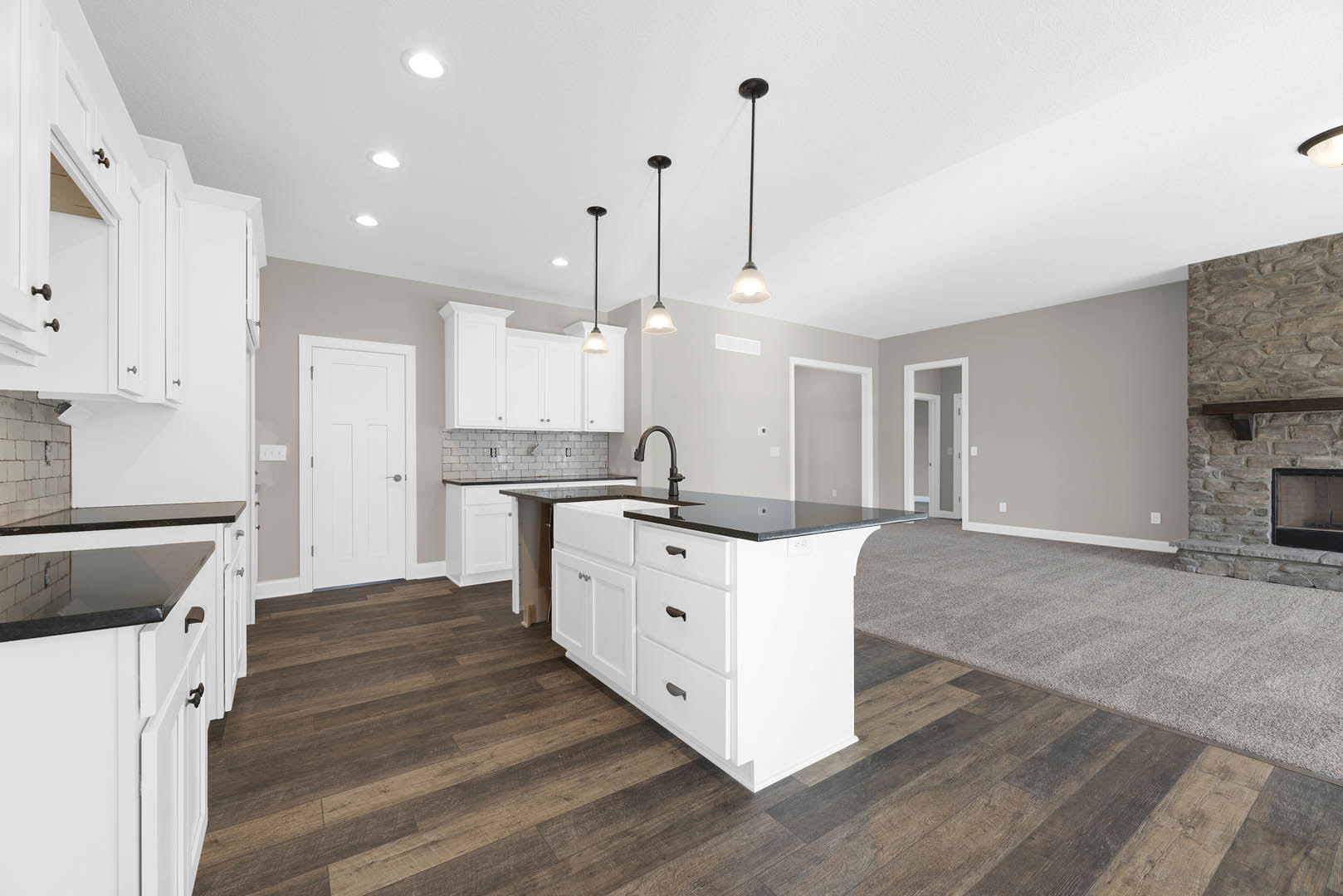 Open kitchen and living room featuring white cabinetry, white kitchen island with black countertop, stainless steel sink, tiled floor, fireplace with window insert, multiple white