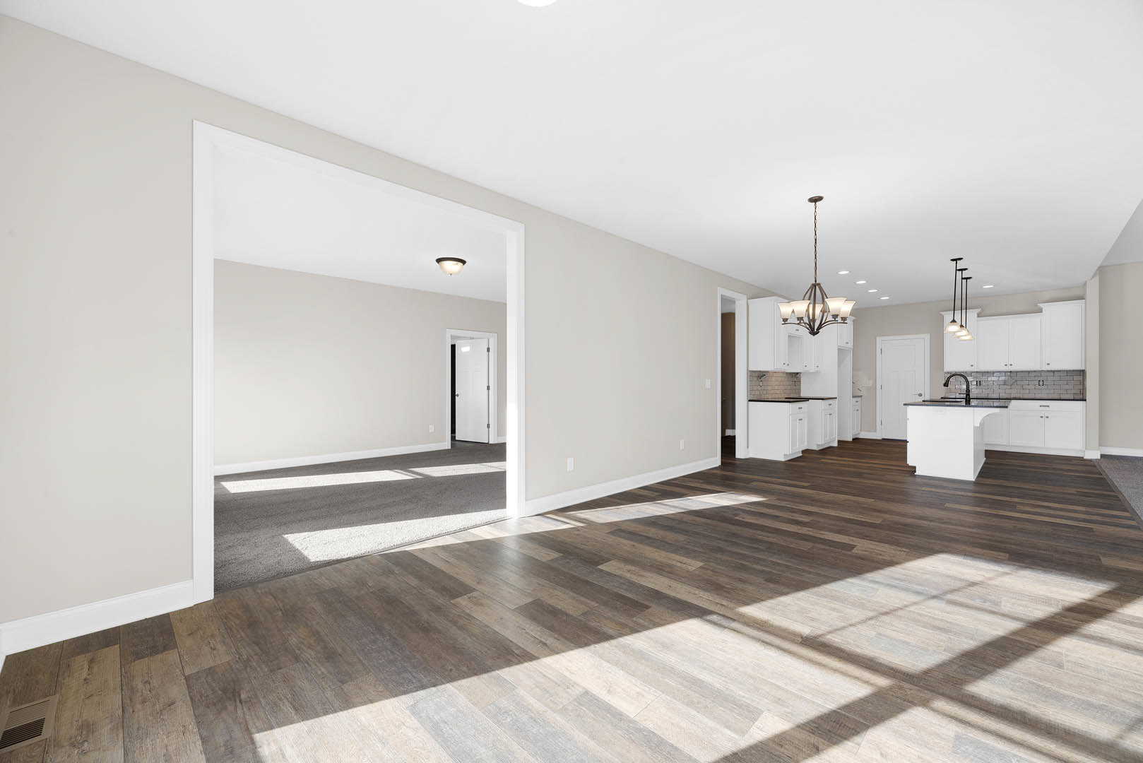 Spacious open-plan room featuring wood laminate flooring, white kitchen cabinetry with black countertops, modern ceiling light fixture, and a white door with black trim.