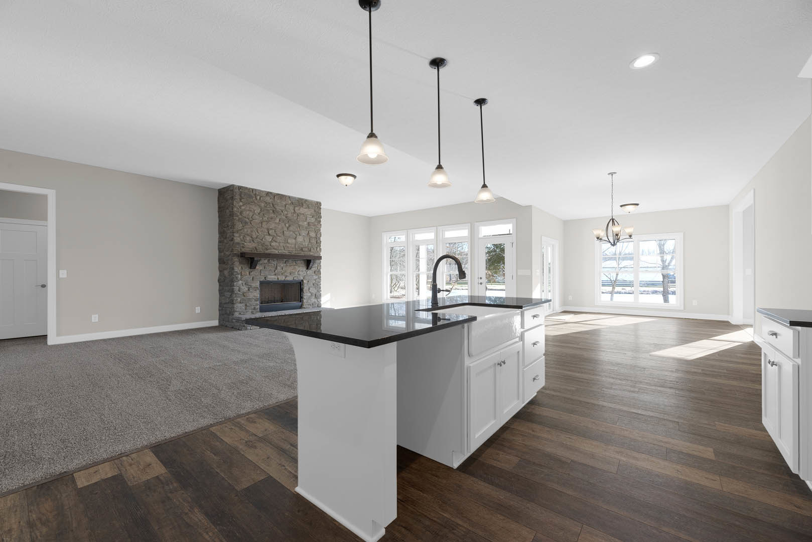 Kitchen with stone fireplace, black countertop island, white cabinetry, stainless steel appliances, wood shelf above fireplace, light hardwood flooring