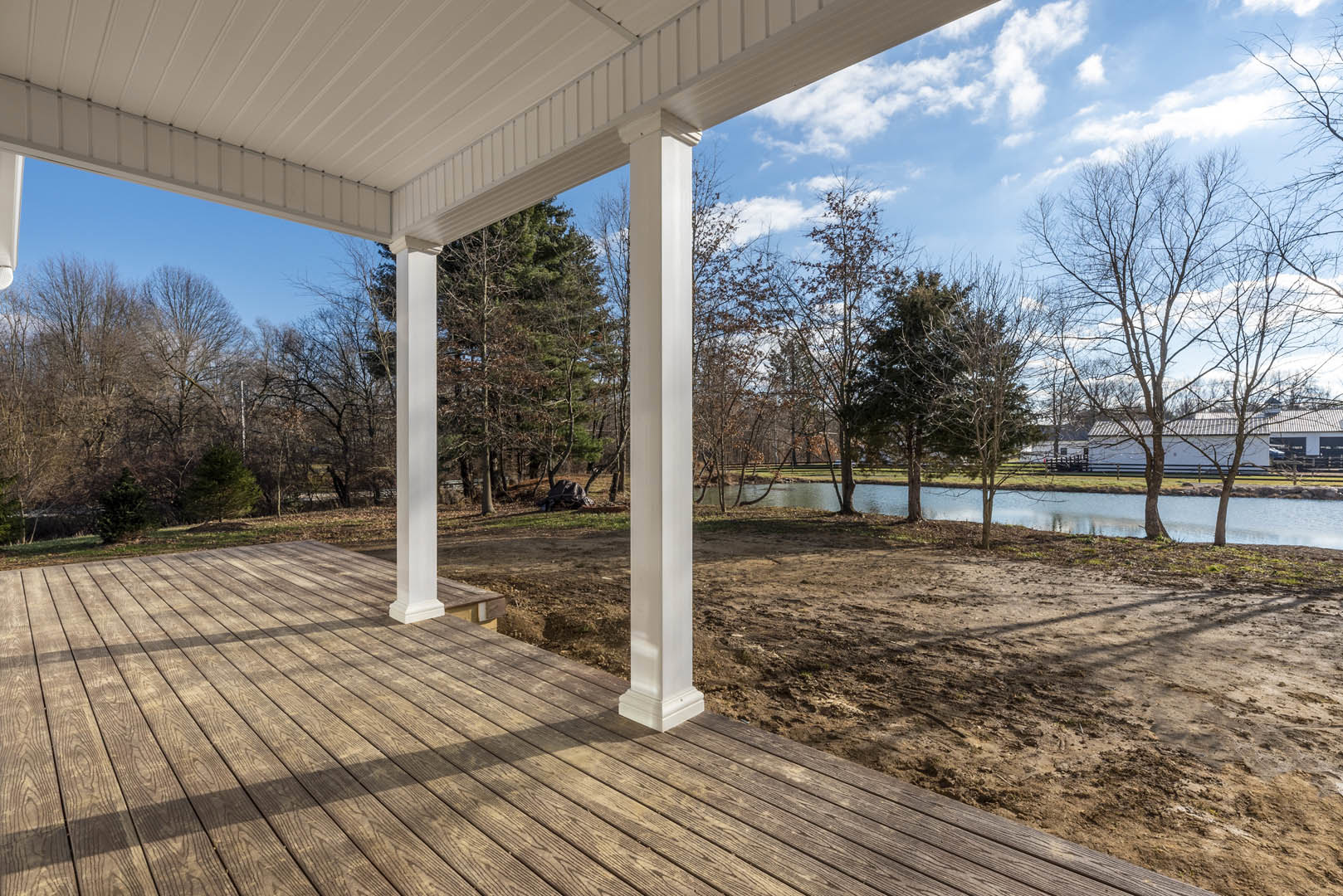 Wooden porch with white pillars and metal roof, overlooking a pond and trees in the background