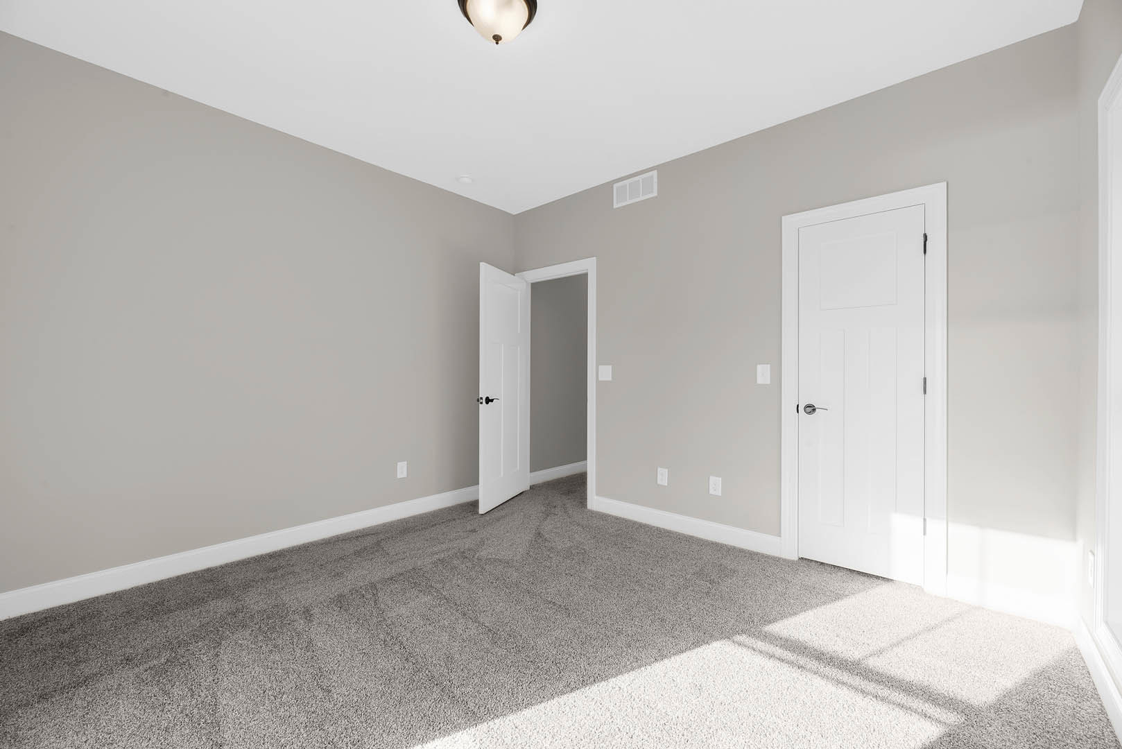 Bedroom with plush beige carpet, white paneled doors featuring silver and black handles, white walls, crown molding, and a ceiling-mounted light fixture with a frosted shade