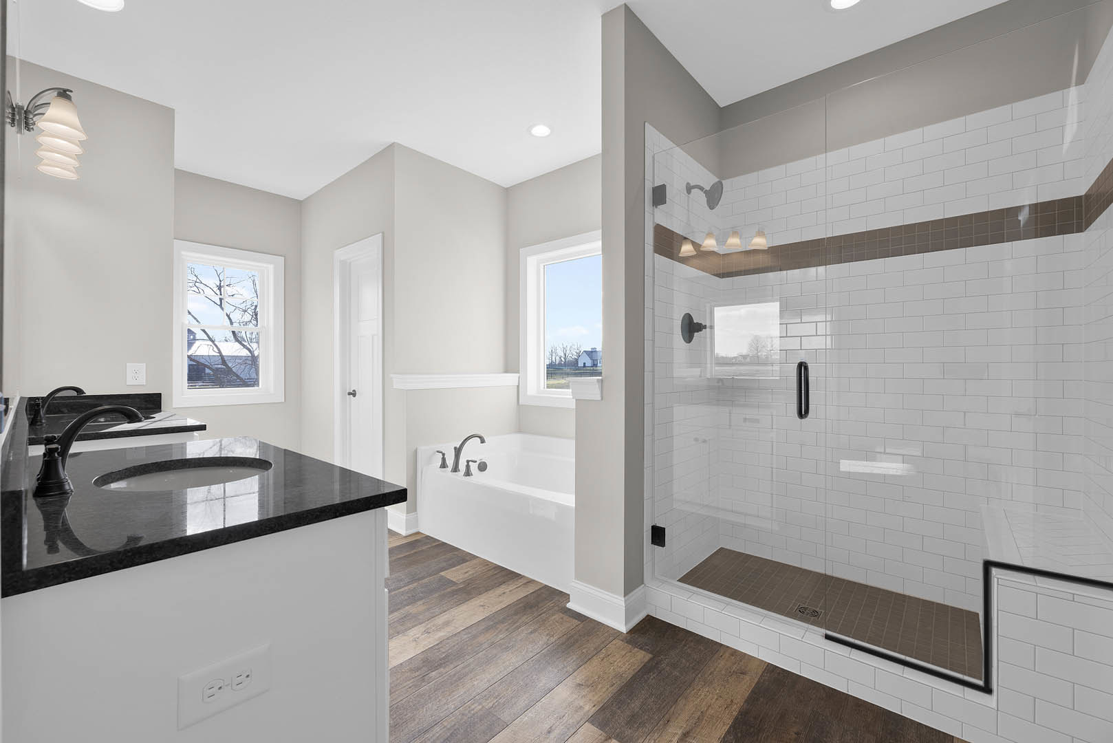Bathroom featuring a glass-enclosed shower, freestanding tub, white countertop with sink and chrome faucet, large window overlooking a house and trees, and a ceiling light fixture