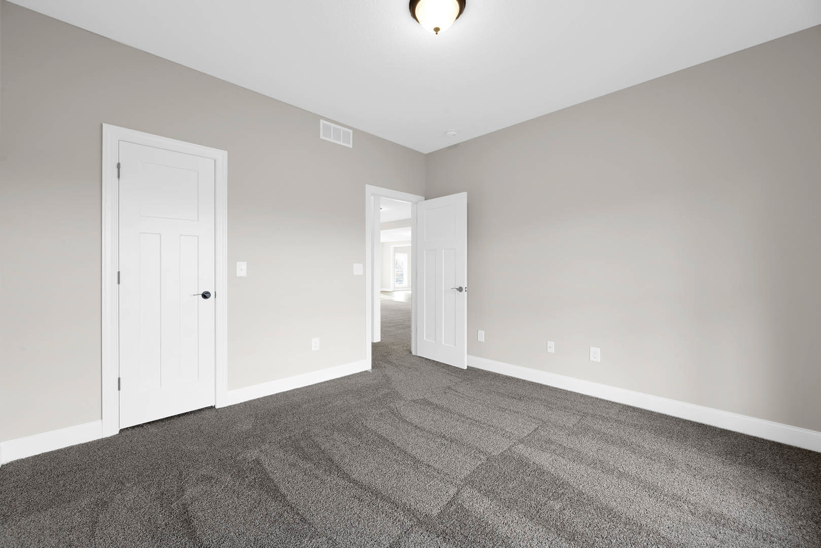 Bedroom with plush beige carpet, white paneled doors featuring black handles, white-framed window, smooth plaster walls, and ceiling molding.