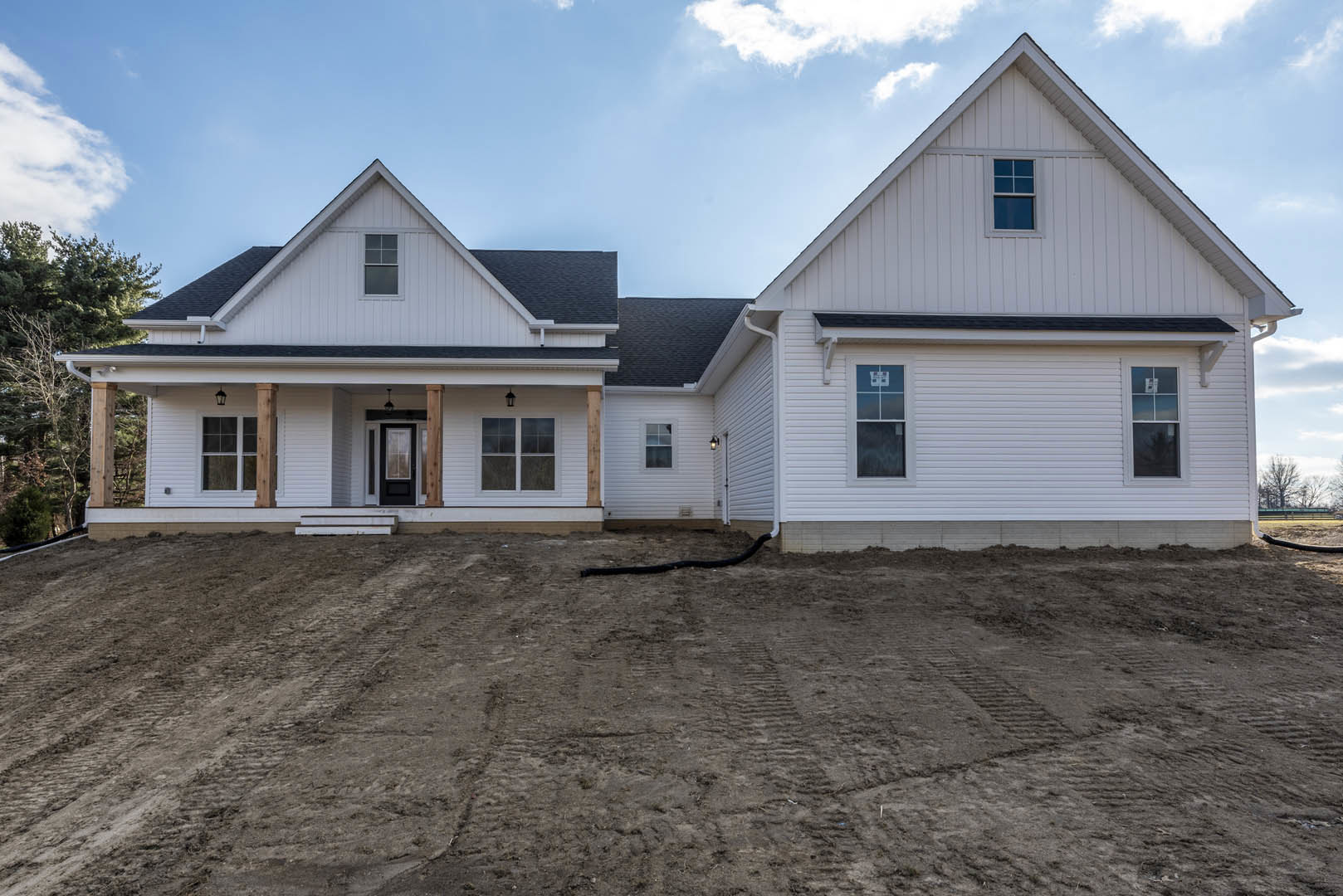 White house with square-paned windows and white frames, set against a blue sky; dirt hill and tire tracks visible in the foreground.