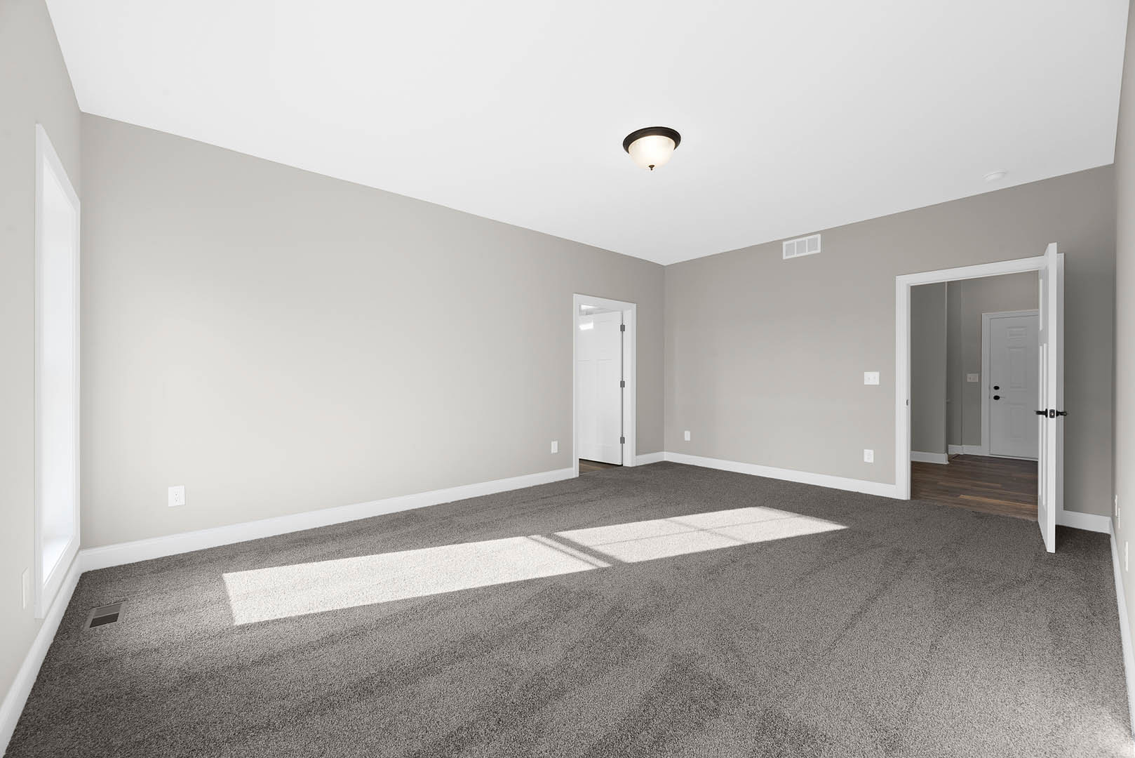 White door with black handle on a carpeted floor, white walls, round black-framed ceiling light fixture