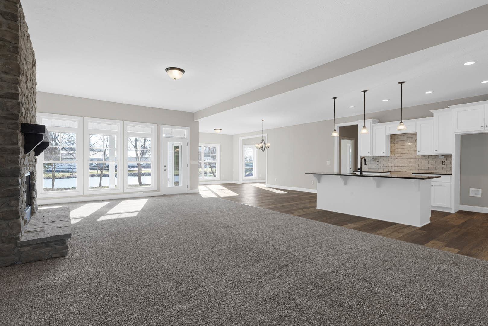 Spacious open floor plan featuring a kitchen with black countertops, white walls, and a bar area; adjoining living room with carpet flooring, white plaster ceiling, and modern
