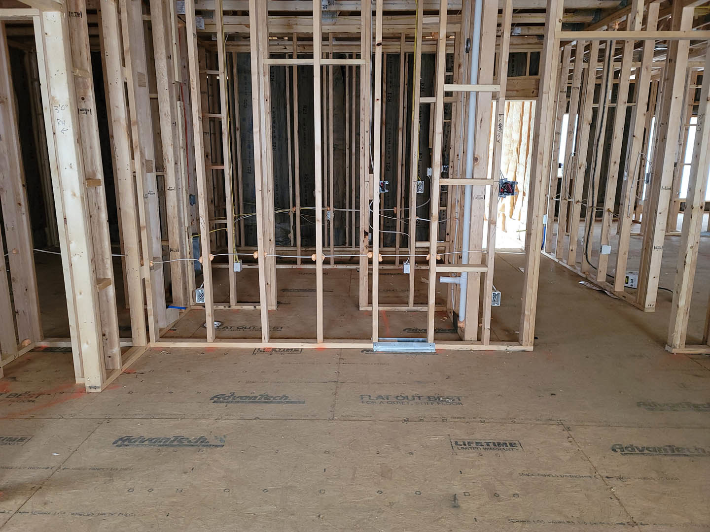 Exposed wood framing and wall studs inside a house under construction, with a black metal grate resting on sandy subfloor