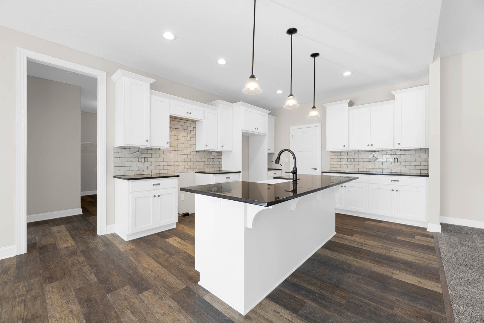 Kitchen featuring a black countertop island, white cabinetry, stainless steel sink, tile backsplash, and light wood flooring