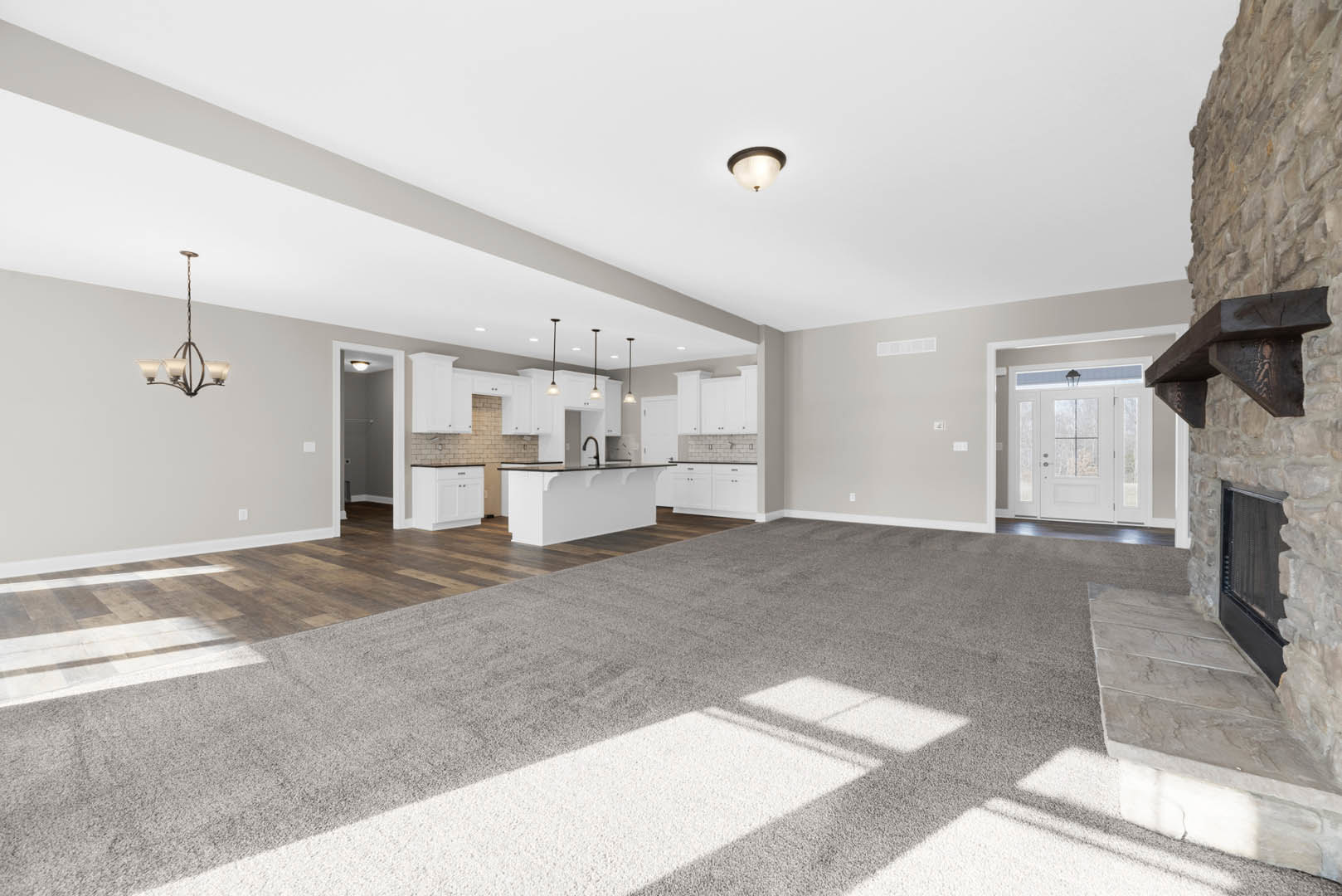 Spacious open floor plan featuring a modern kitchen with white cabinetry, a living room with neutral carpeting, a white door with glass panes, a closet with white walls, and a