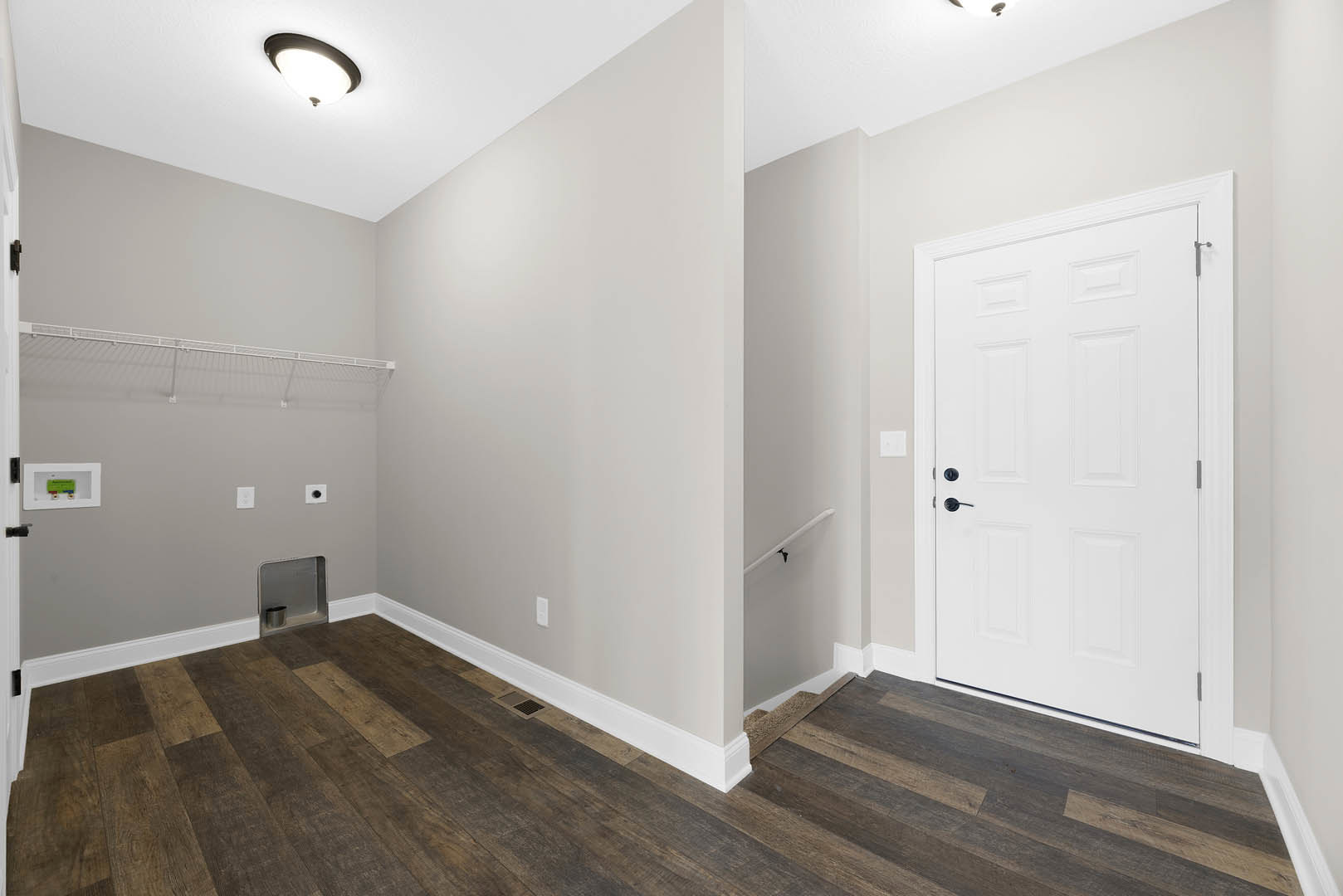 Hallway with wood flooring and white baseboards, two white doors with black handles, ceiling light fixture, green and blue card in a white frame on the wall