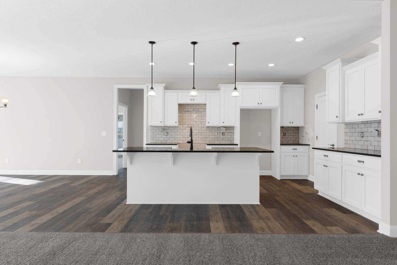 Kitchen with wood flooring, central island featuring black countertop, white cabinetry, stainless steel sink, pendant lighting, and white walls.