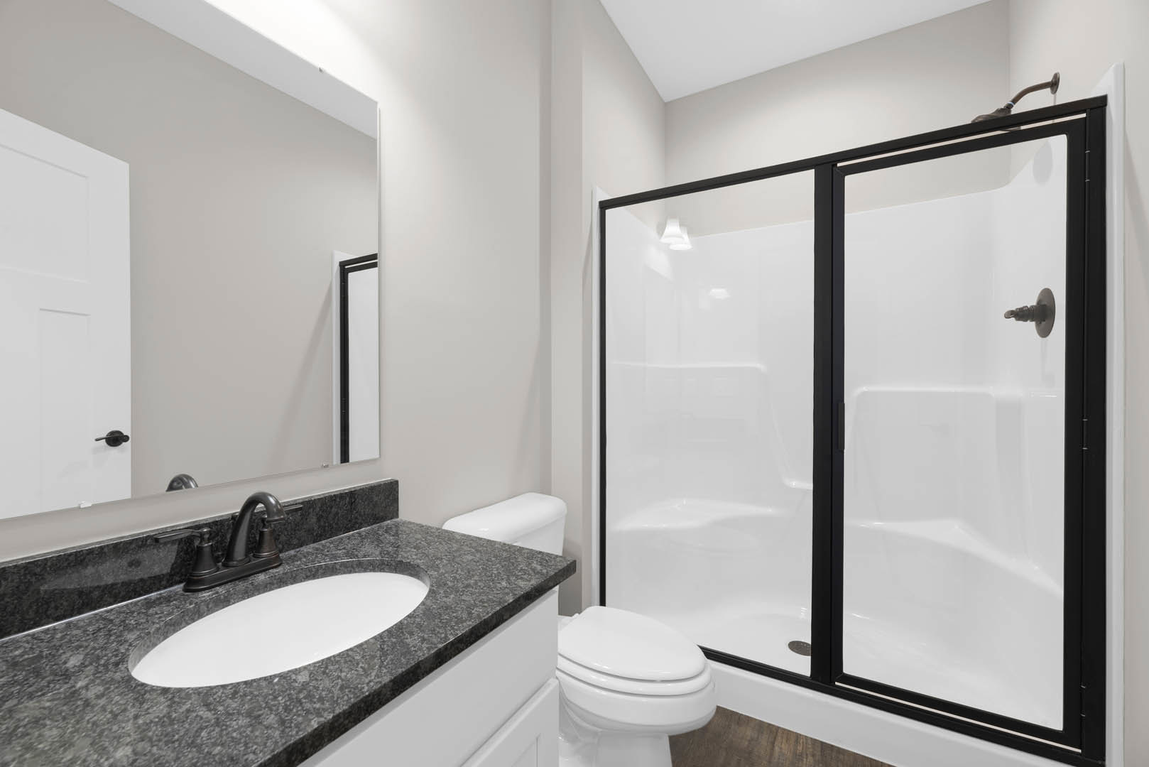 Modern bathroom featuring a glass-enclosed shower, white porcelain sink with chrome faucet, closed white toilet, light-colored tile walls, and a white door