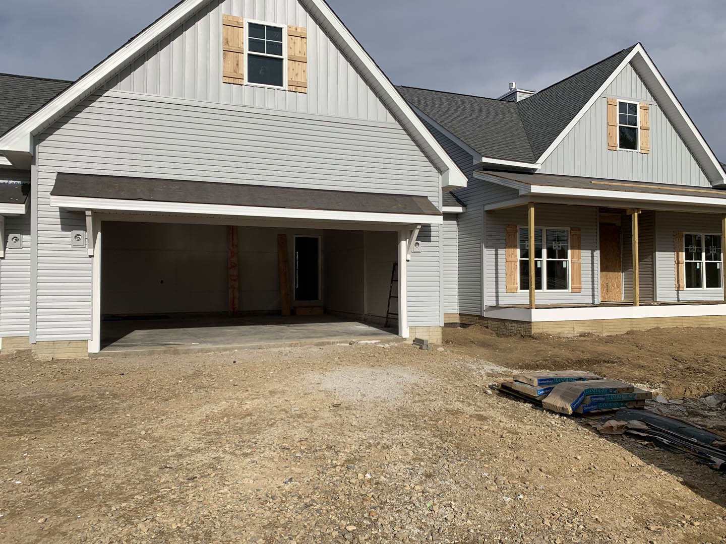 Partially built house with white-framed window, exposed siding, dirt path lined with rocks and gravel, and construction materials scattered on the ground