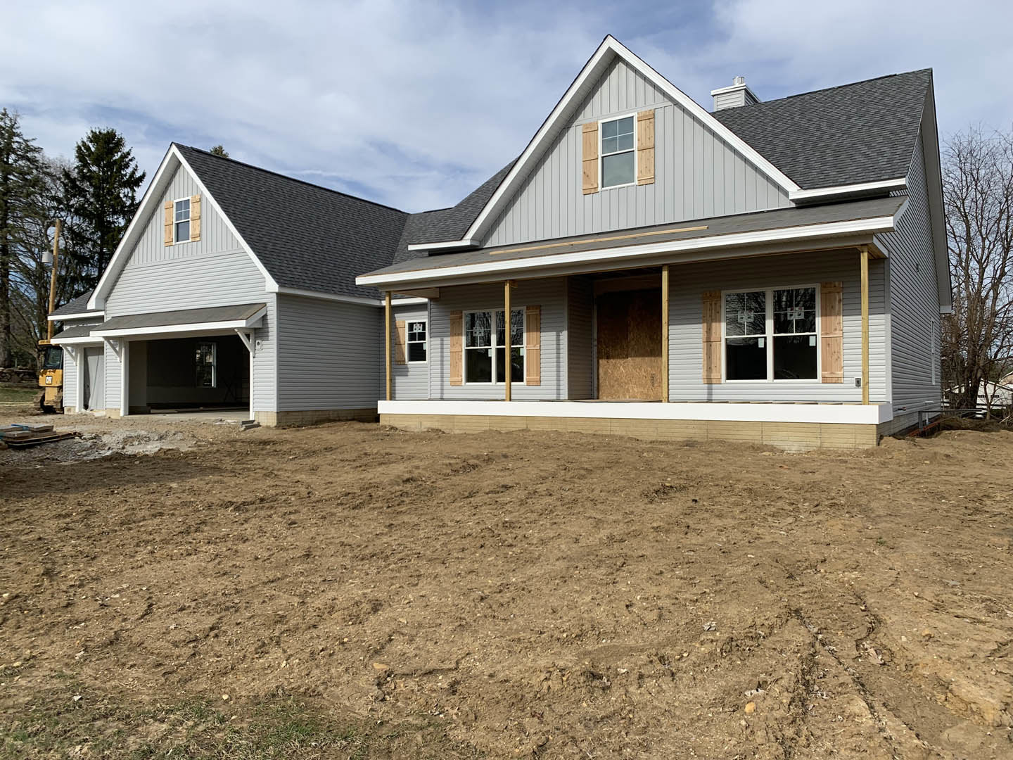 Two-story house with light siding, open door, shuttered windows, and dirt yard under partly cloudy sky