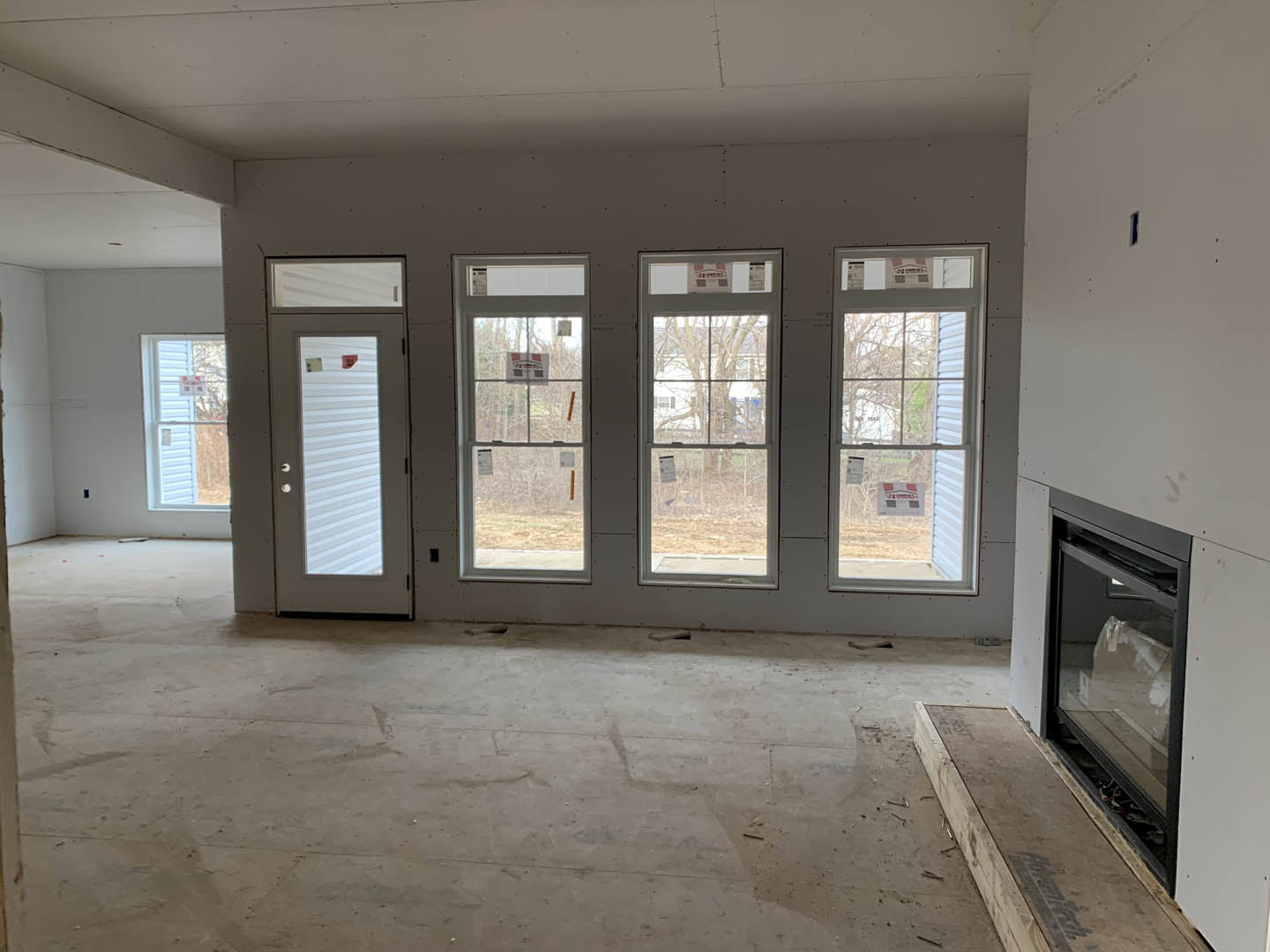Living room with large windows, white plaster walls, hardwood flooring, and a stone fireplace.
