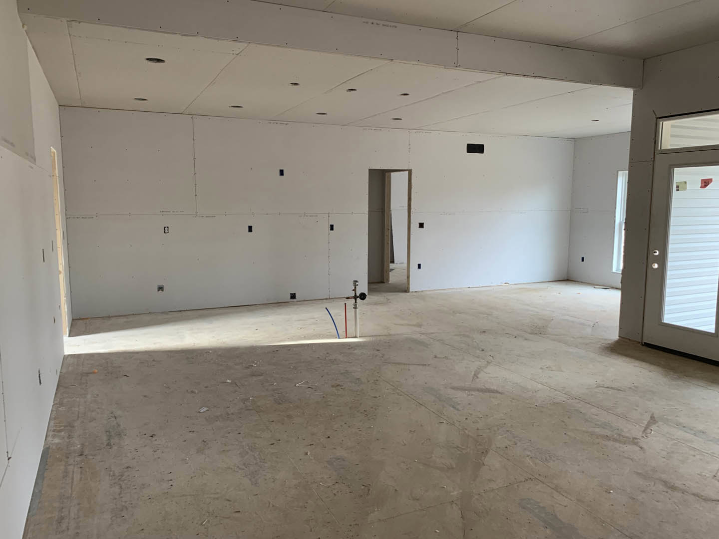 White plaster walls, concrete floor with exposed pipes, wood ceiling beam, window and door, unfinished ceiling with visible holes
