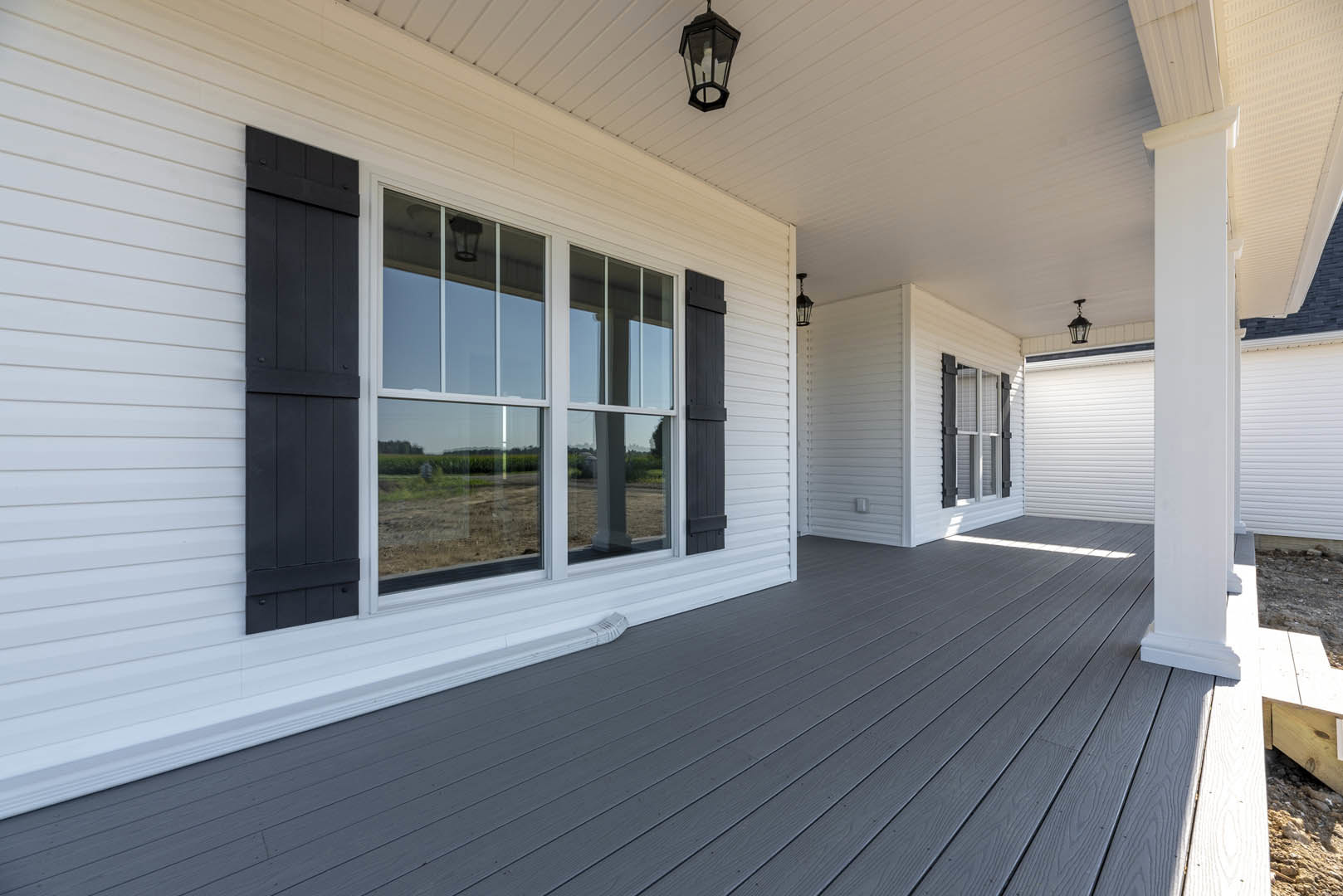White siding exterior with black shutters, wood deck, large window, and porch lamp.