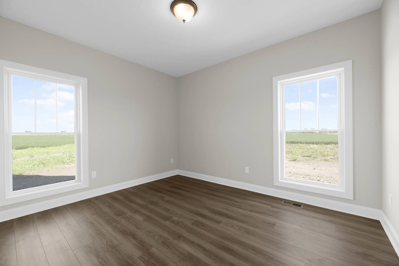 Spacious room with wood flooring, white baseboards, large windows overlooking a field, and a round ceiling light fixture