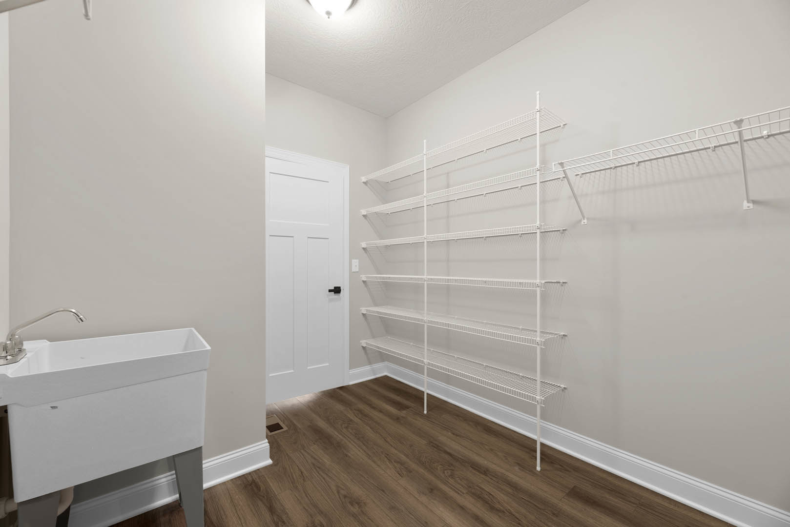White built-in shelves beside a white door with black handle, white sink and chrome faucet, wood flooring with white trim, and plaster walls in a bathroom.