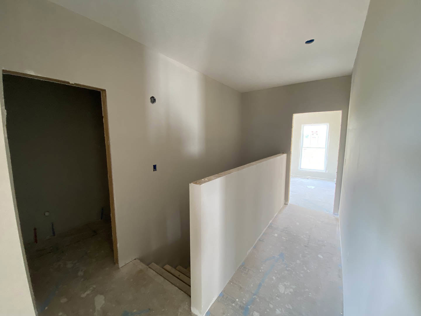 Hallway with white plaster walls, blue accent wall, wood flooring, staircase with white railing, window with white frame letting in natural light, and dark-colored door.