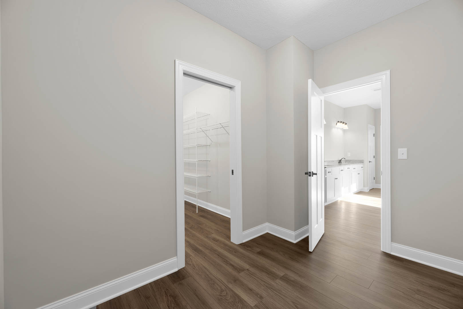 Wood flooring and white walls in a bright room, featuring a white door frame and built-in closet shelves