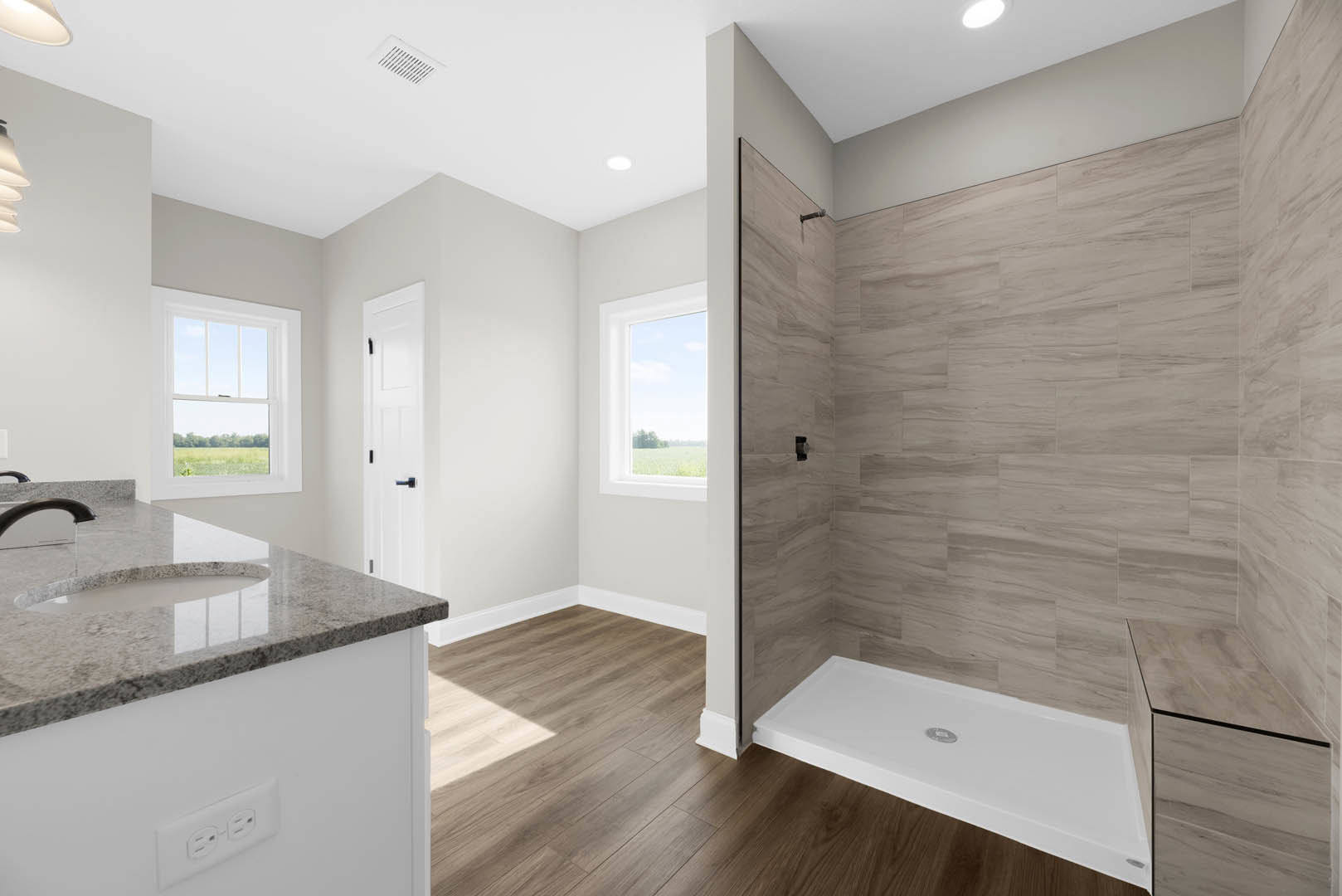 Modern bathroom featuring a glass-enclosed tile shower, white rectangular sink with chrome faucet, stone countertop, and a window with a white frame overlooking a grassy field