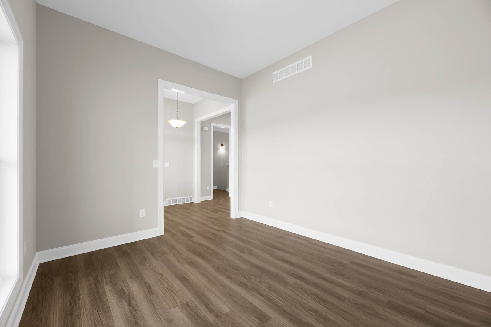 Wood flooring in a room with white walls, white ceiling featuring a vent and recessed light, door with molding visible.