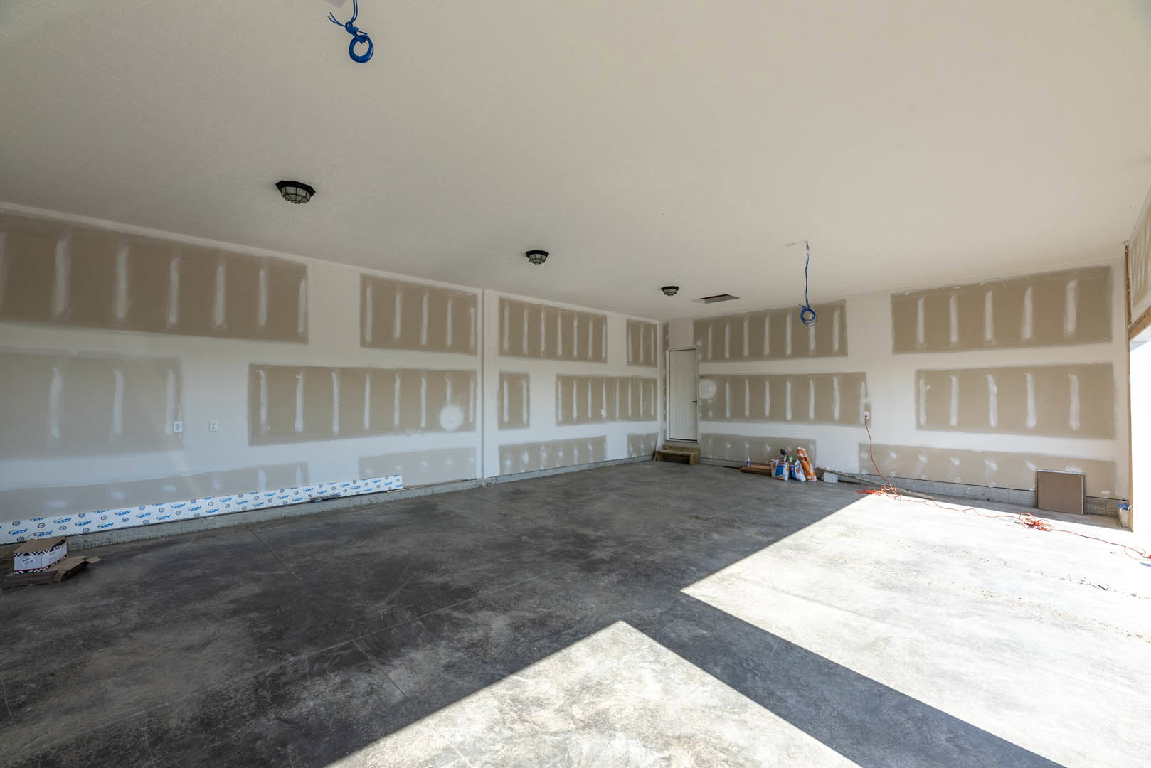 White walls and concrete flooring in a minimalist room, featuring a white door with a black handle and subtle shadows across the floor.