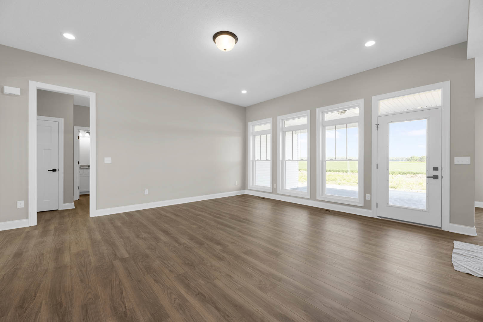 Wood floor with white walls, white door featuring black handle, ceiling light fixture, white cloth on floor, view of grassy field through door