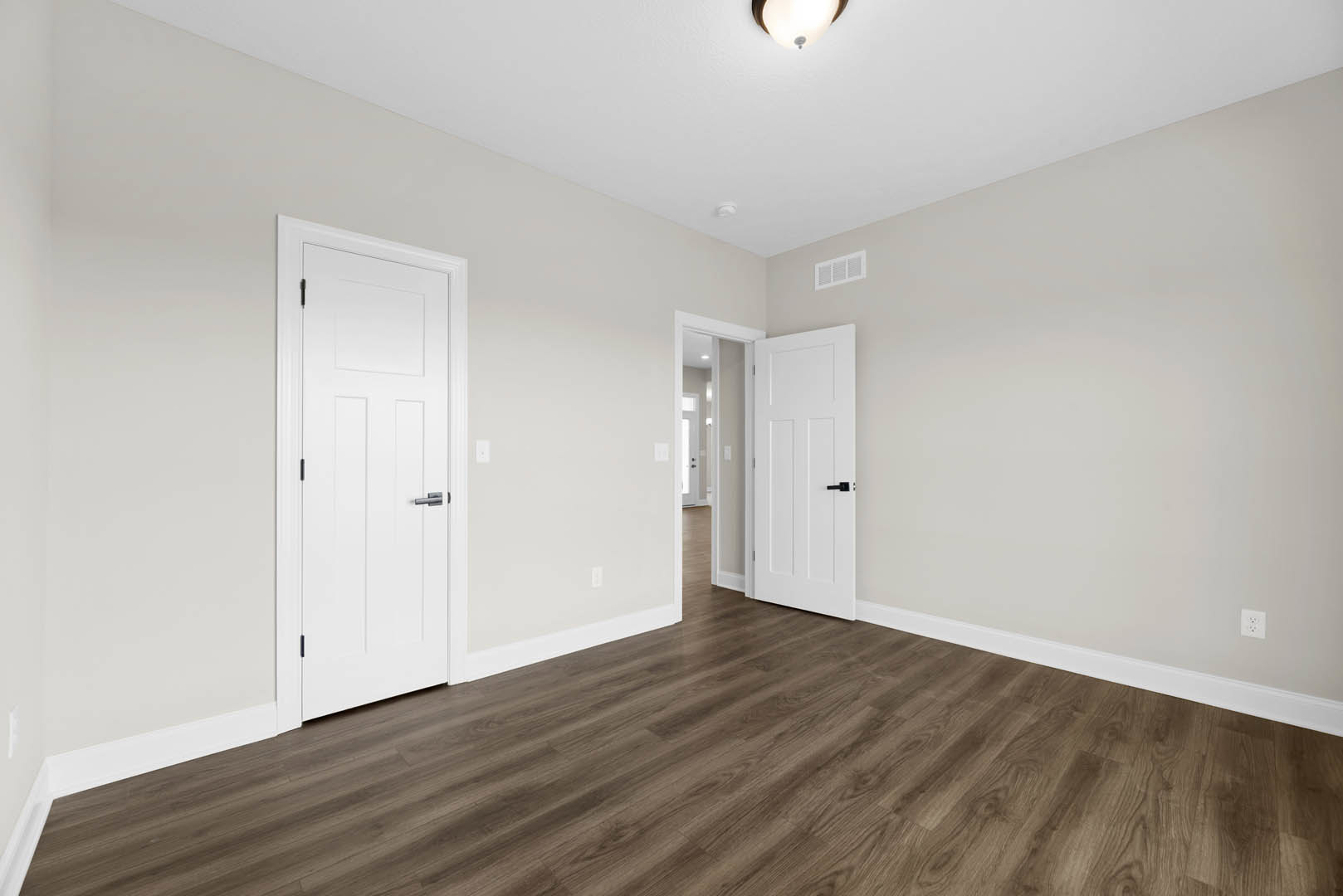 White paneled doors with black handles, hardwood flooring, white walls, and a wall vent in a bright interior room