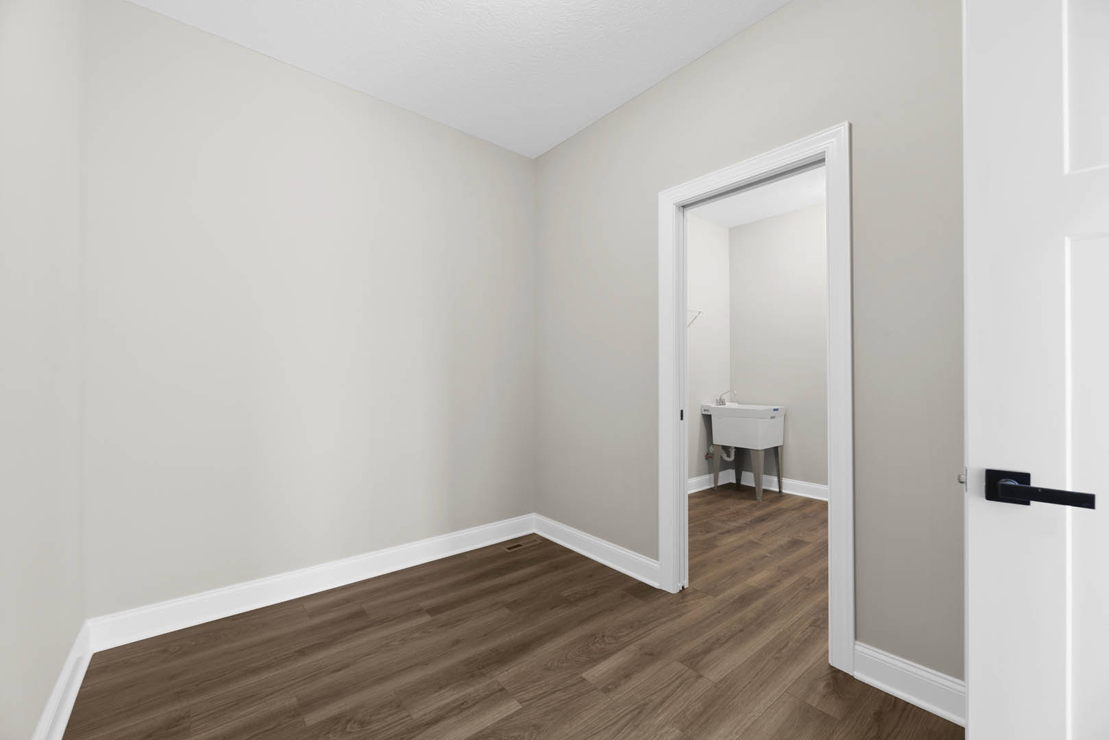 Wood flooring with white baseboards, open door leading to bathroom featuring white sink and cabinetry, neutral walls, and ceiling with recessed lighting