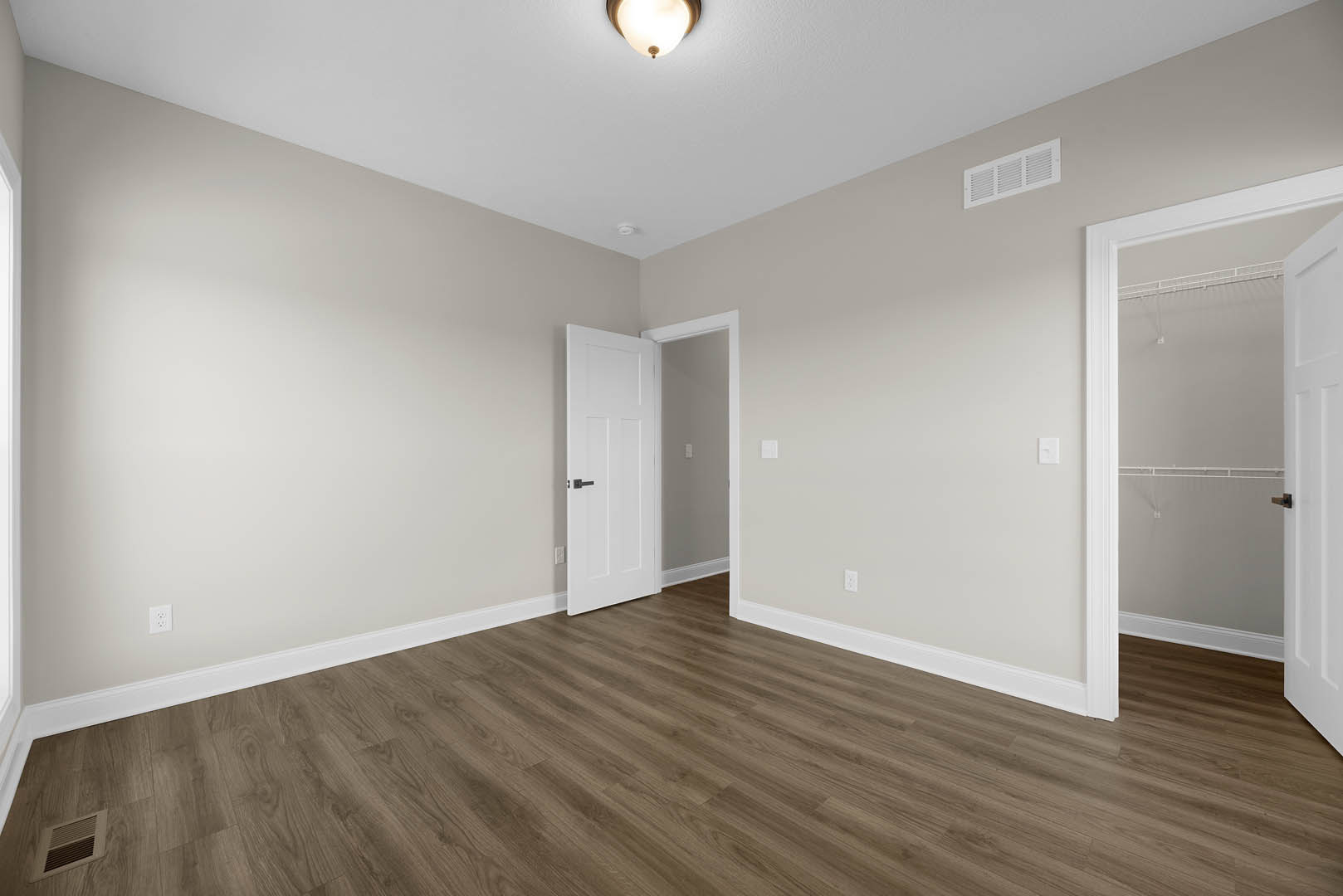 White paneled door with black handle opens to a closet, wood laminate flooring, white plaster walls, ceiling vent, recessed light.