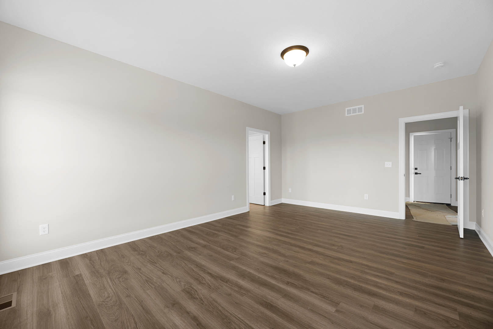 Wood flooring in a room with white walls, a white door featuring black handles, and a modern ceiling light fixture; person standing on a table.
