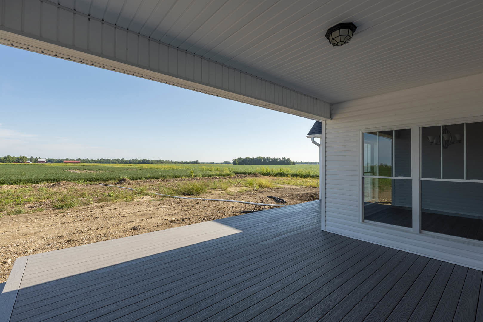 Large white house with composite siding and black trim, expansive grassy lawn, wooden porch with hose, windows, and a close-up of roof and exterior light fixture.