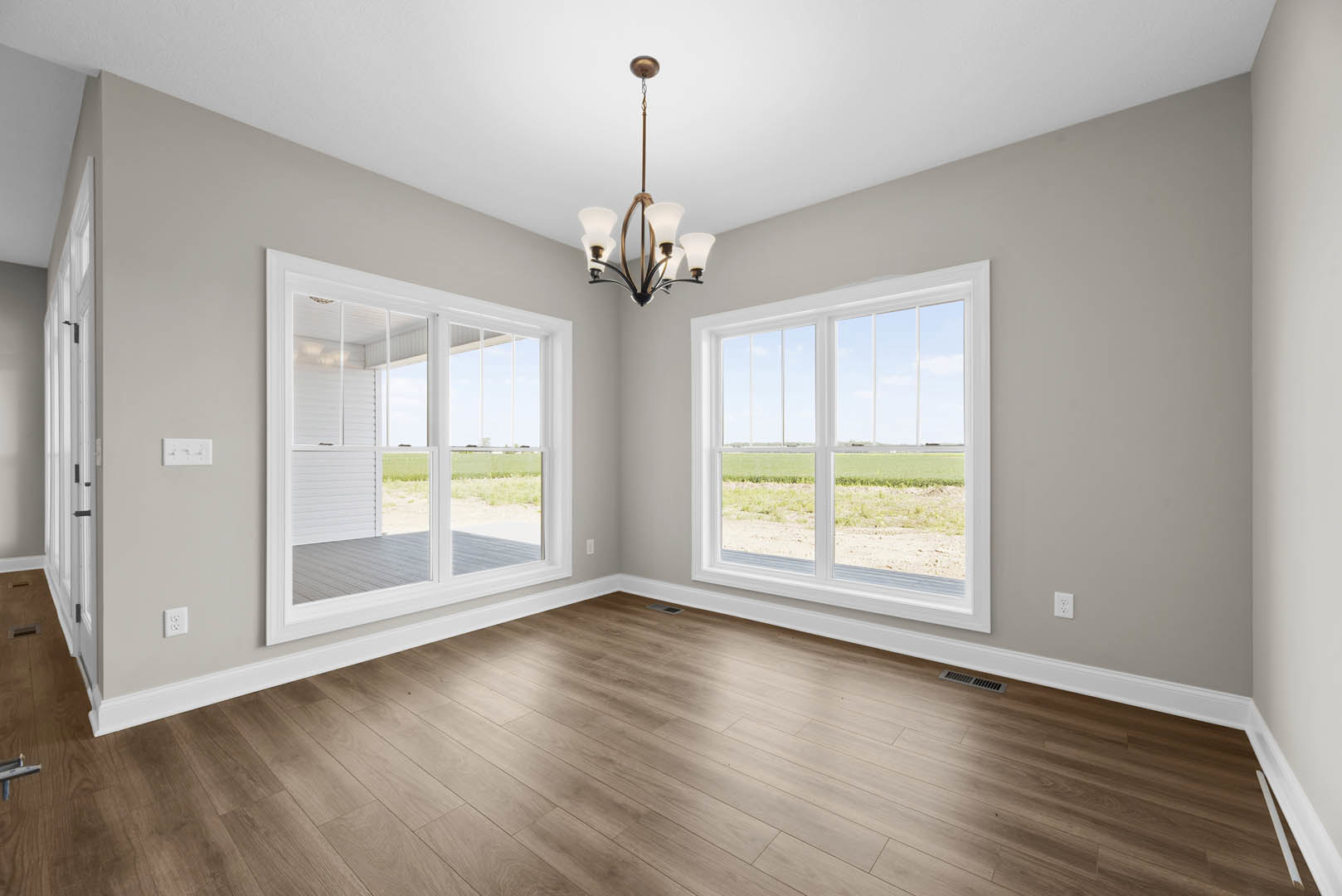 Chandelier hanging from ceiling above hardwood floor, large windows with views of grassy field, white plaster walls