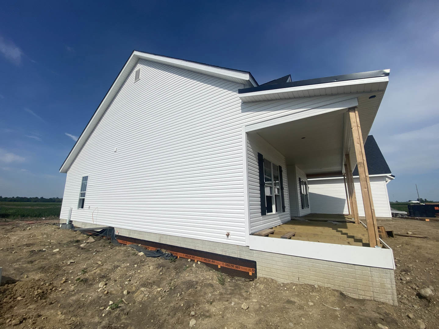 White custom home under construction with exposed dirt foreground, black-framed windows, and clear blue sky overhead