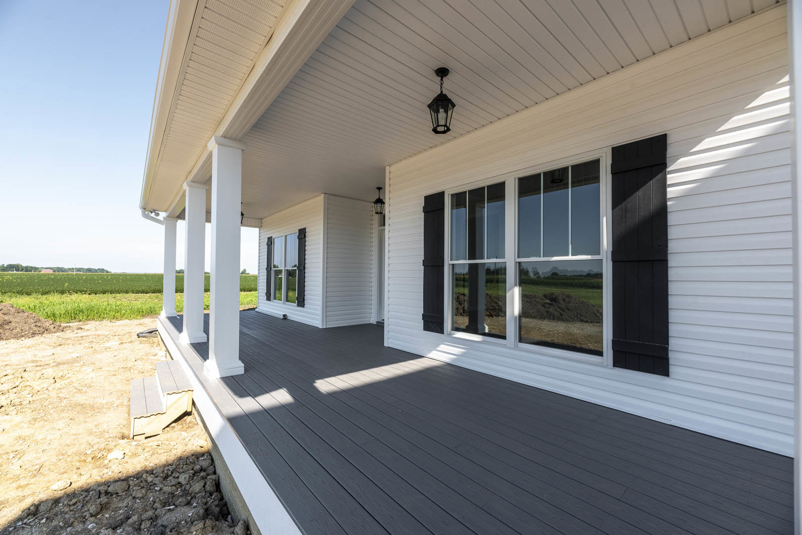 White siding house with black-framed windows and door, spacious grassy lawn, covered porch, and visible roof details.
