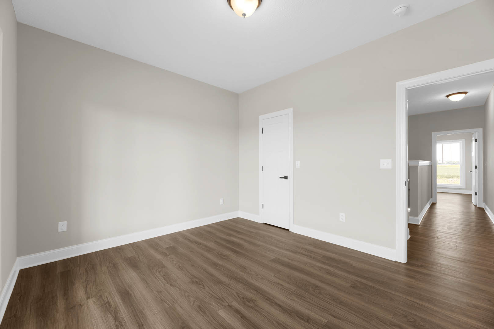Open room with wide plank wood flooring, white walls, modern ceiling light fixture, and white door with black handle leading to grassy field.