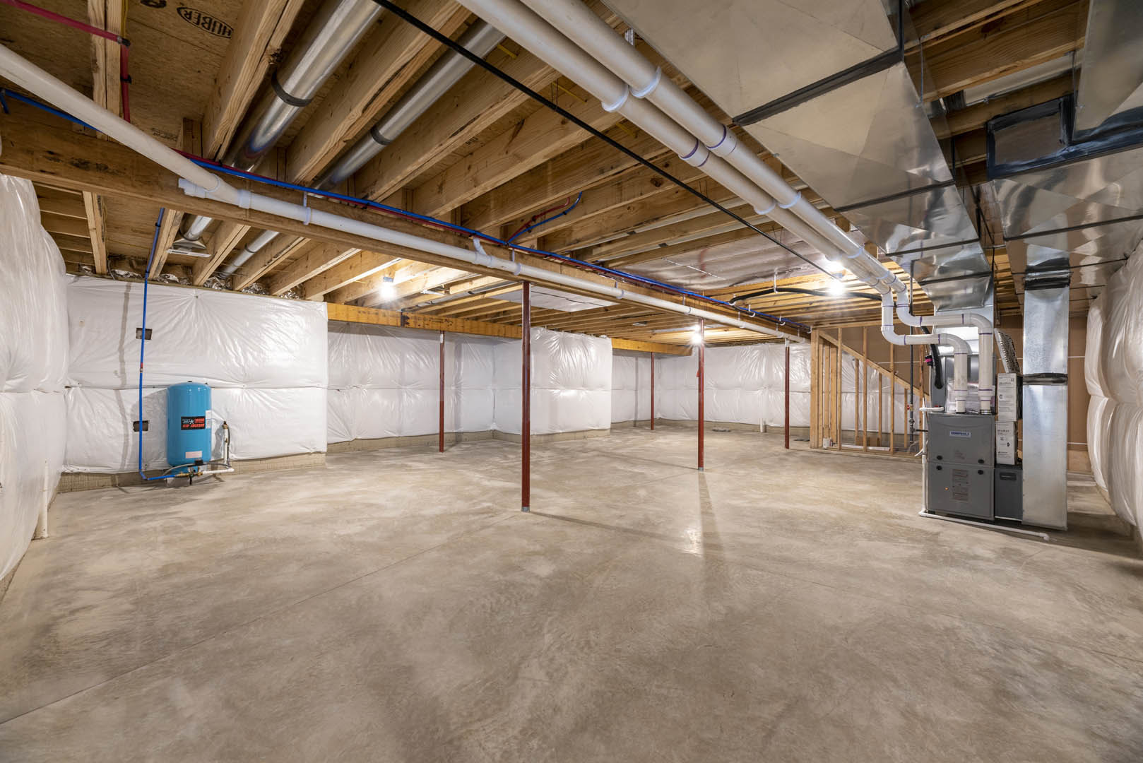 Basement with exposed ceiling pipes, concrete floor, red steel poles, blue cylinder with black sticker, grey electrical box, and visible logo.