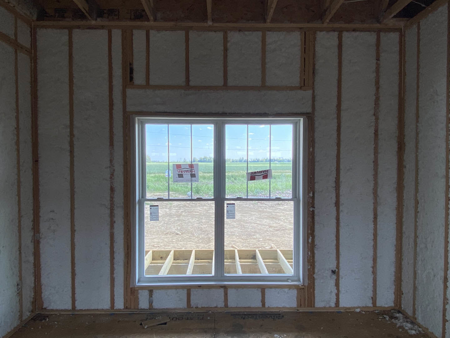 Large window with white trim overlooking grassy field, sunlight streaming onto neutral painted walls and light wood floor.