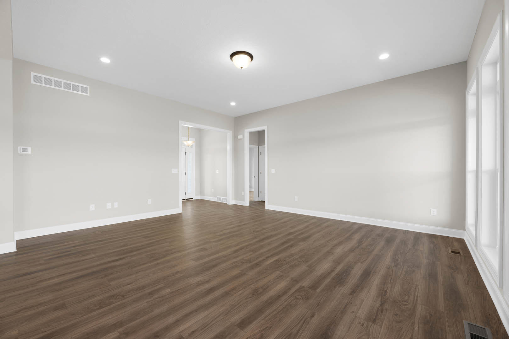 Hardwood flooring, white plaster walls, ceiling-mounted light fixture, wall vent, window with trim