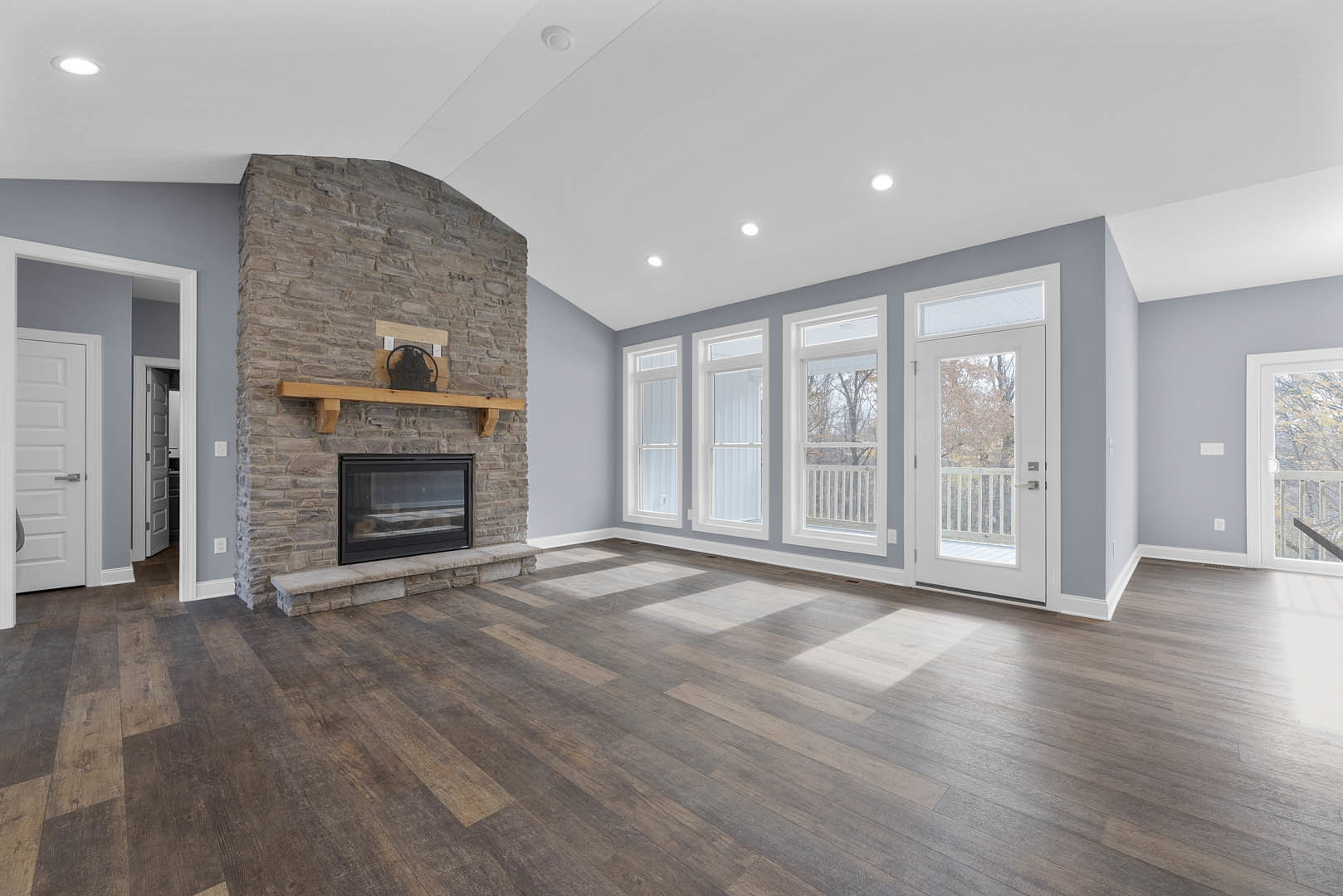 Living room with hardwood flooring, brick fireplace featuring a wood mantel, exposed wood ceiling beam, white door with glass window, and plaster walls.