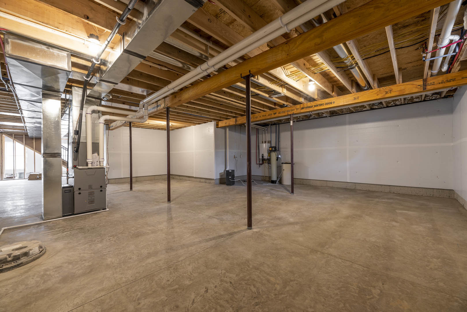 Concrete floor and wood plank ceiling with exposed metal pipes, structural pole, and electrical box in an unfinished basement room.