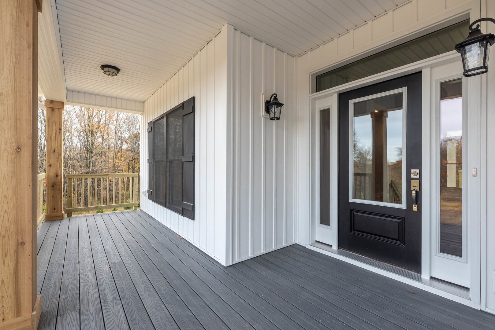 Front porch with wooden railing, screened door, ceiling-mounted light fixture, and trees visible in the background