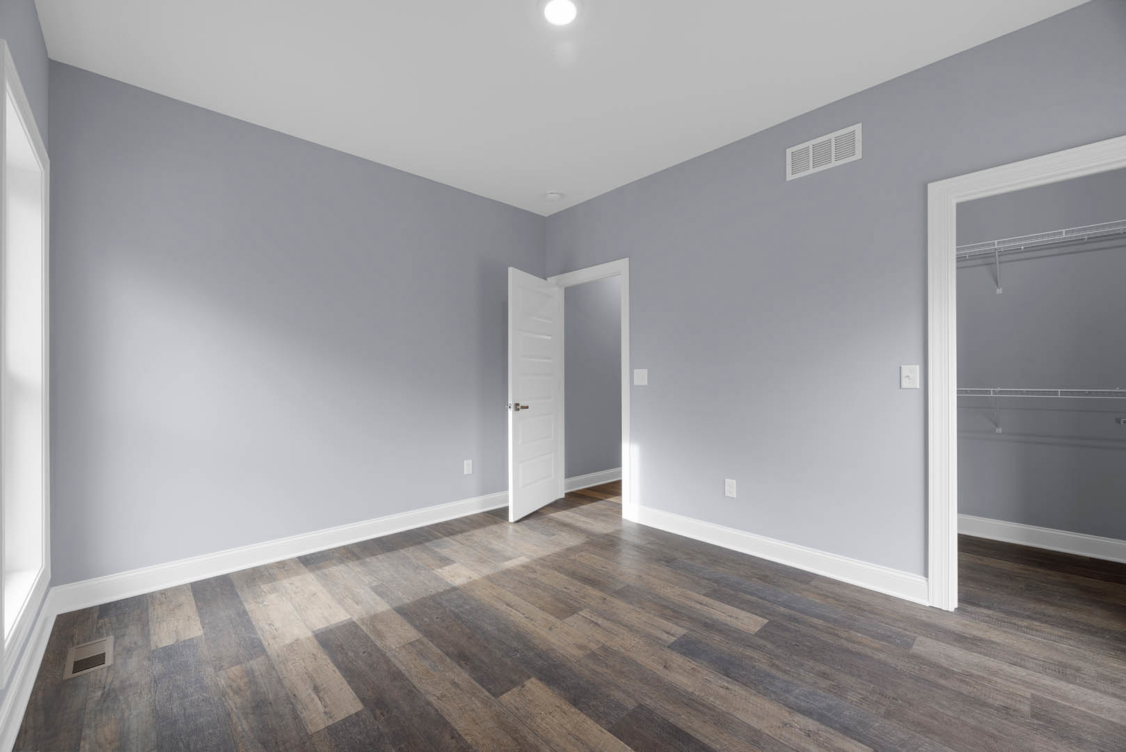 Open white door with chrome handle on wood laminate floor, white walls, wall vent, and black-framed rectangular object